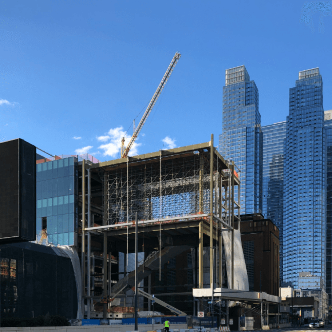 Street level view of the Javits Center expansion showing cranes, scaffolding and a building behind the construction zone.